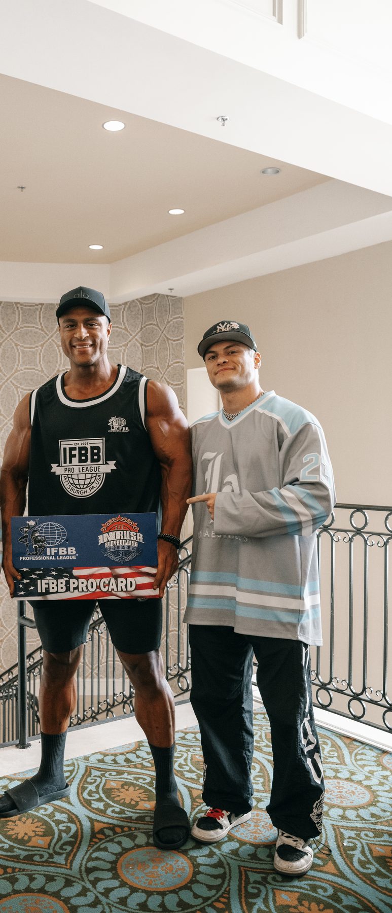 Client and Jake holding an IFBB Pro Card in the hallway