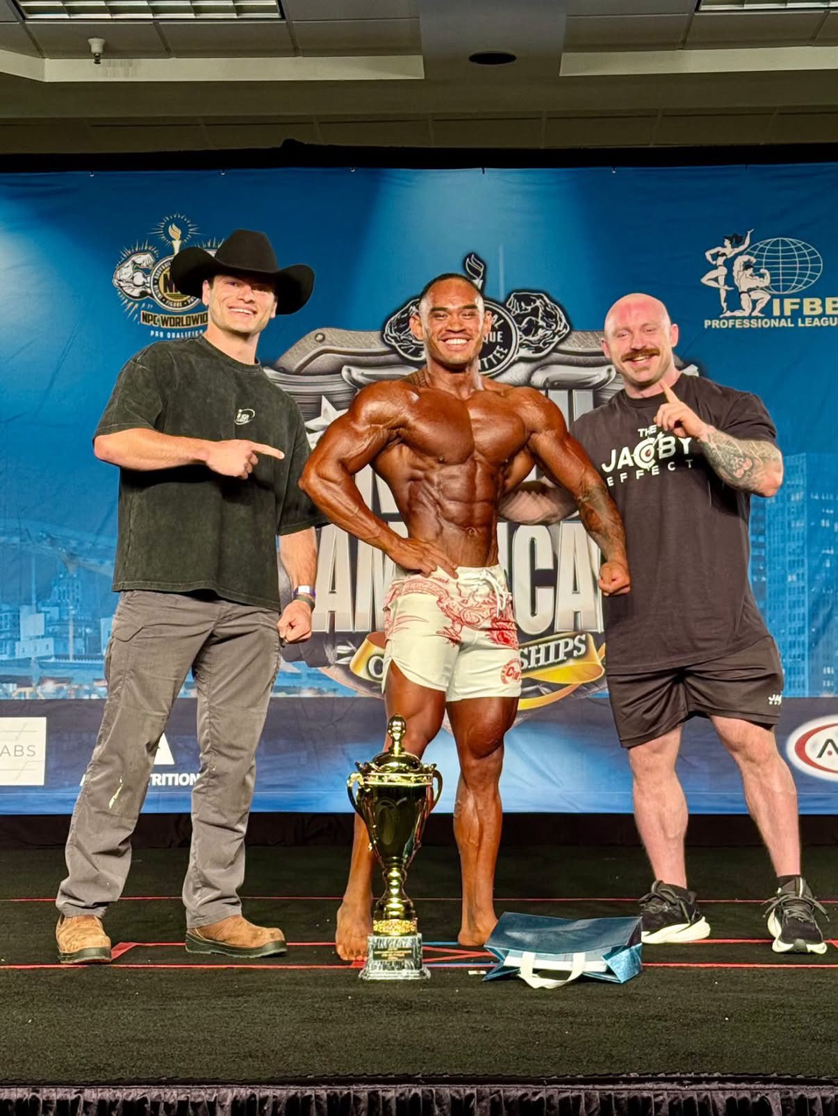 Client hitting a front pose on the North American Championships stage with Jake and his coach
